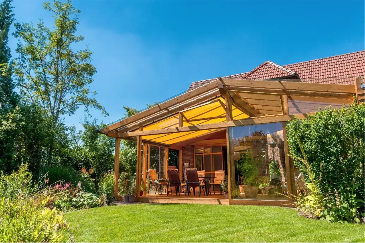 Ein moderner Wintergartenanbau mit Glasfront und gelbem Sonnensegel bietet tolle anbau wintergarten ideen. Gemütliche Sitzmöbel laden zum Verweilen ein.