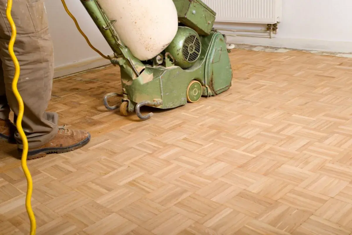 Mann schleift Parkett mit einer Maschine. Der Boden wird für eine neue Oberflächenbehandlung vorbereitet.