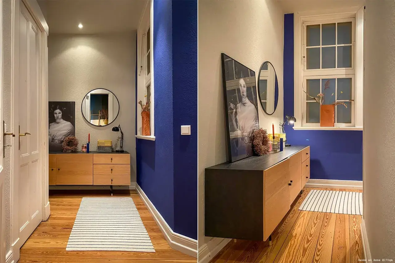 Flur mit Wand in tiefem Indigo, Holzmöbel, Spiegel und Kunstwerk. Ein Streifenmuster auf dem Teppich ergänzt die Szene.