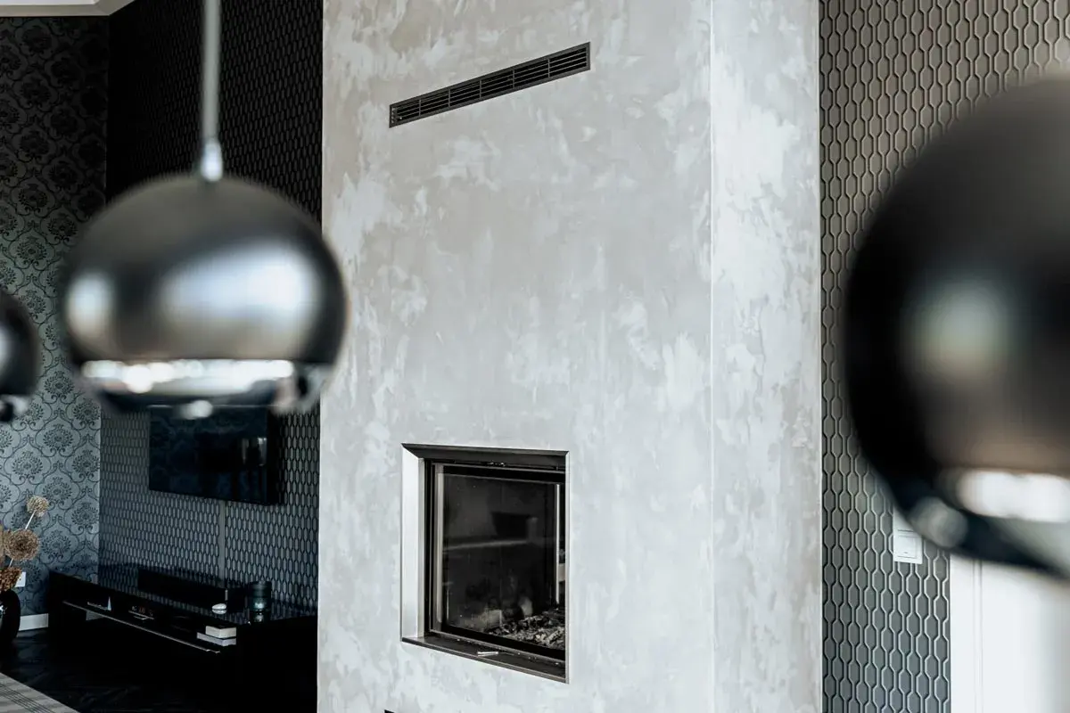 Edler Kamin mit Wischtechnik Wand in Grau. Daneben eine Wand mit geometrischem Muster und ein Teil einer Hängeleuchte.