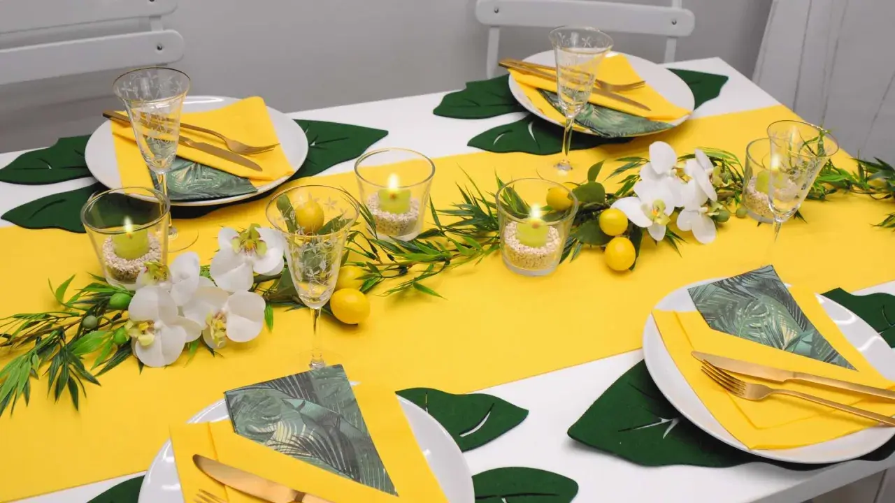 Sommerliche tischdeko mit zitronen, Orchideen und Kerzen. Gelbe Servietten und goldene Besteckteile runden das Bild ab.