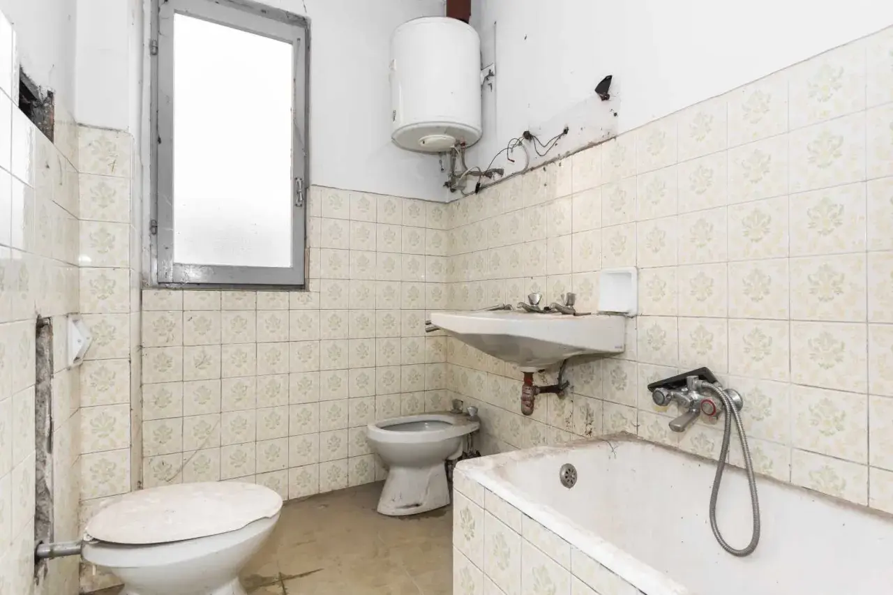 Badezimmer mit veralteten Fliesen, bereit zum Streichen. Toilette, Waschbecken und Badewanne sind sichtbar.