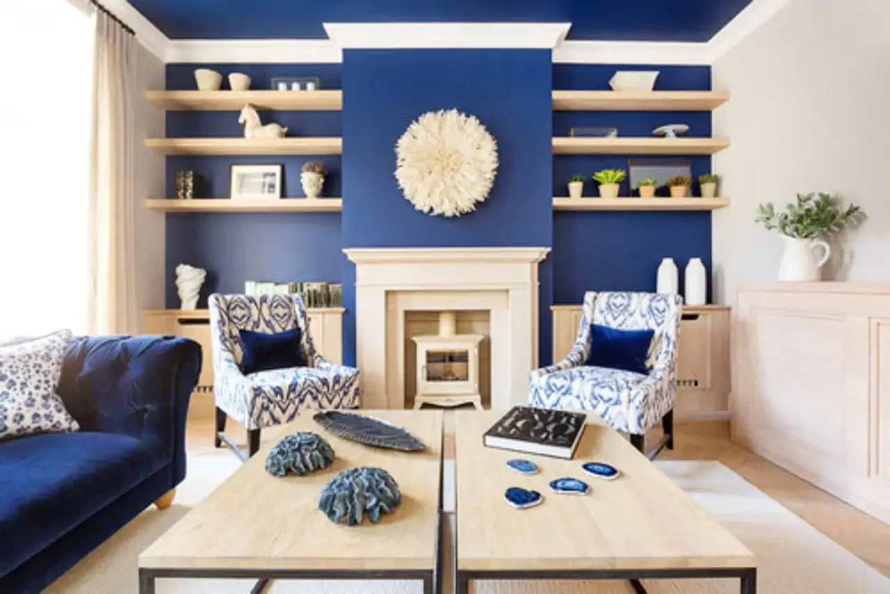 Ein Wohnzimmer mit tiefblauer Decke und Wand, die eine harmonische Einheit bilden. Ein Kamin und zwei Sessel mit blau-wei&szlig;em Muster stehen im Mittelpunkt.