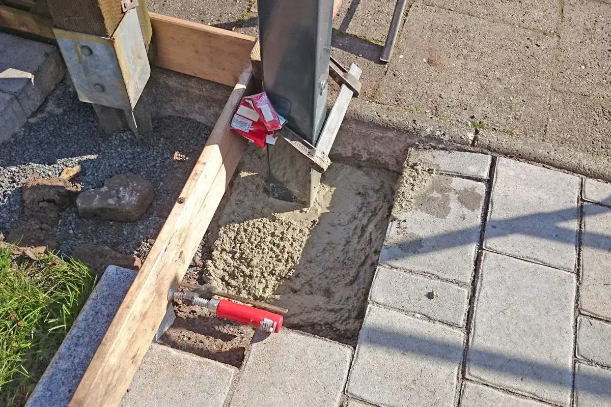 Gartentor einbetonieren: Ein Pfosten wird in frischen Beton gestellt, um Stabilit&auml;t zu gew&auml;hrleisten. Holzschalung und Zement sind sichtbar.