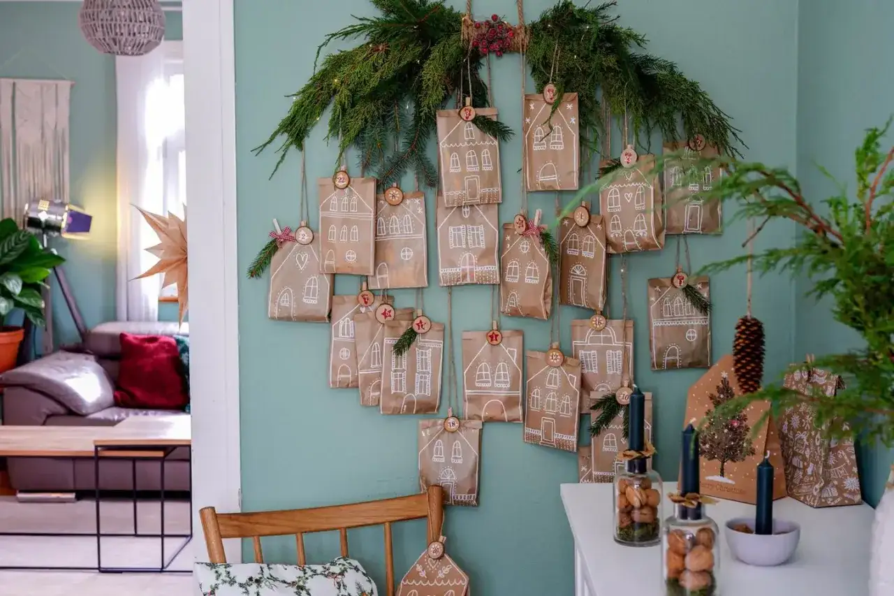 DIY Adventskalender Ideen: Kleine Papiert&uuml;ten mit wei&szlig;en Hausmotiven h&auml;ngen an Tannenzweigen. Jede T&uuml;te ist nummeriert und dekoriert.