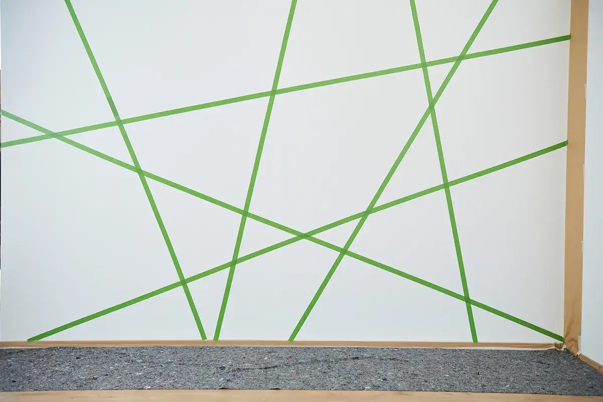 Wand streichen: Muster abkleben f&uuml;r kreative Ideen. Gr&uuml;ne Klebestreifen bilden ein geometrisches Design auf wei&szlig;er Wand.
