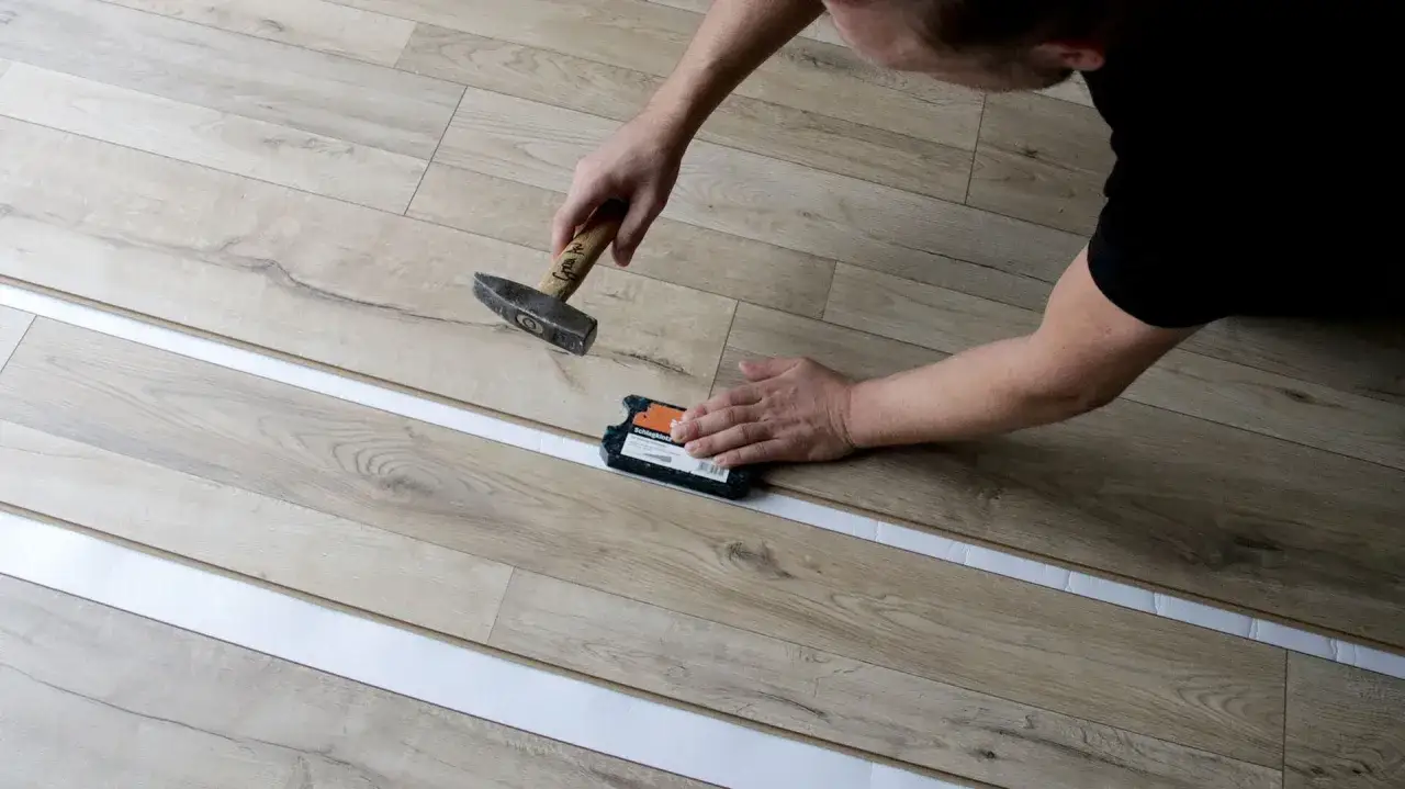 Mann verlegt Laminat mit Hammer und Schlagklotz.