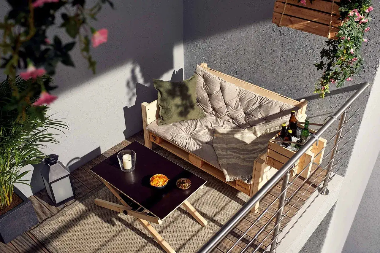 Gemütliche Balkon Ideen: Palettensofa, Holztisch mit Snacks und Getränkekiste. Sonnenschein und Pflanzen schaffen Wohlfühlatmosphäre.