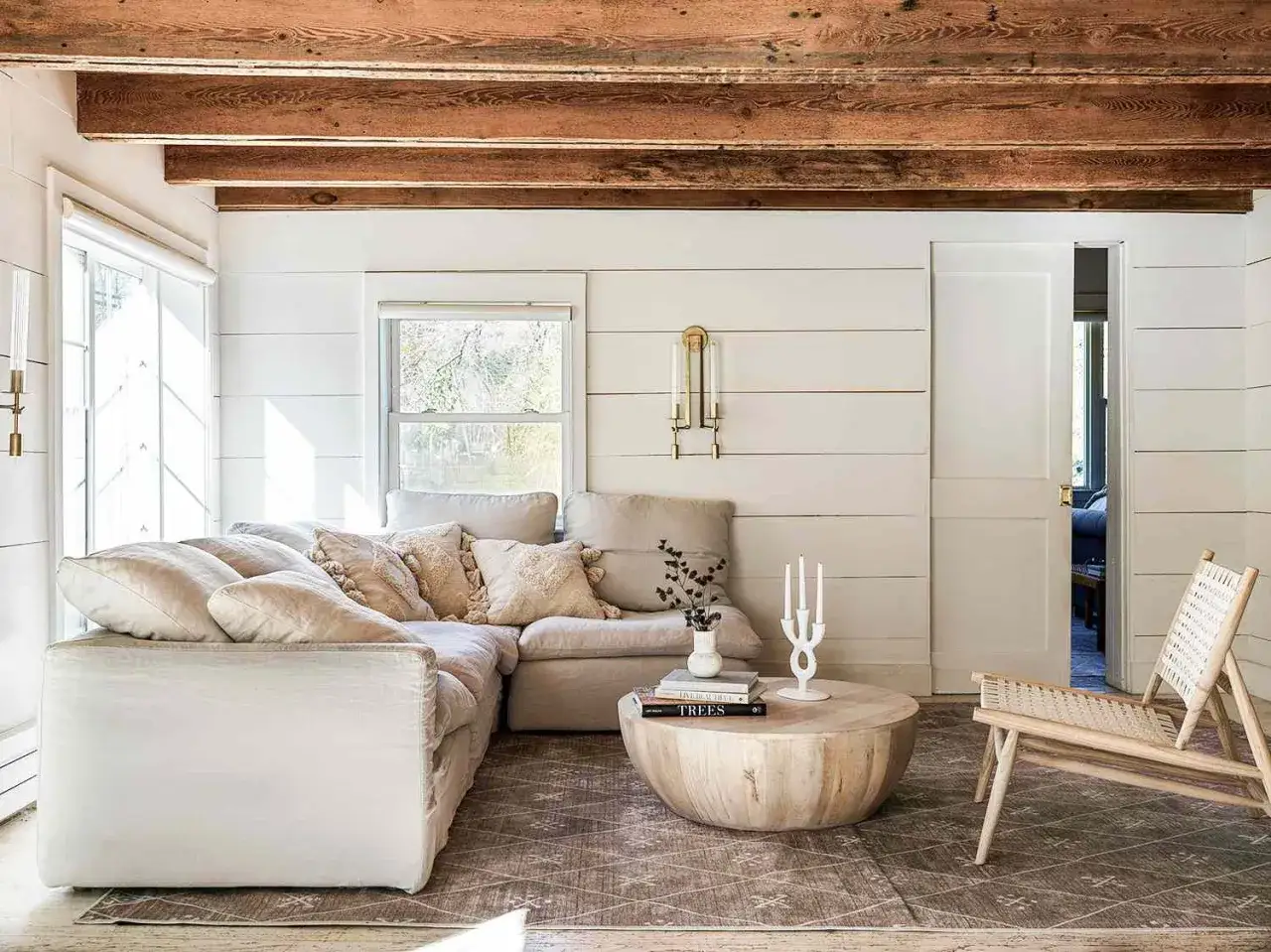 Gem&uuml;tliches Wohnzimmer mit beigem Sofa, Holzbalken und warmen Farben. Ein runder Holztisch steht vor dem Sofa.