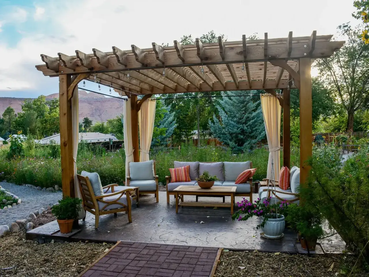 Gem&uuml;tliche Lounge-Ecke unter einer Holzpergola, die zum Pergola selber bauen inspiriert. Mit bequemen Sitzm&ouml;beln und Lichterkette.