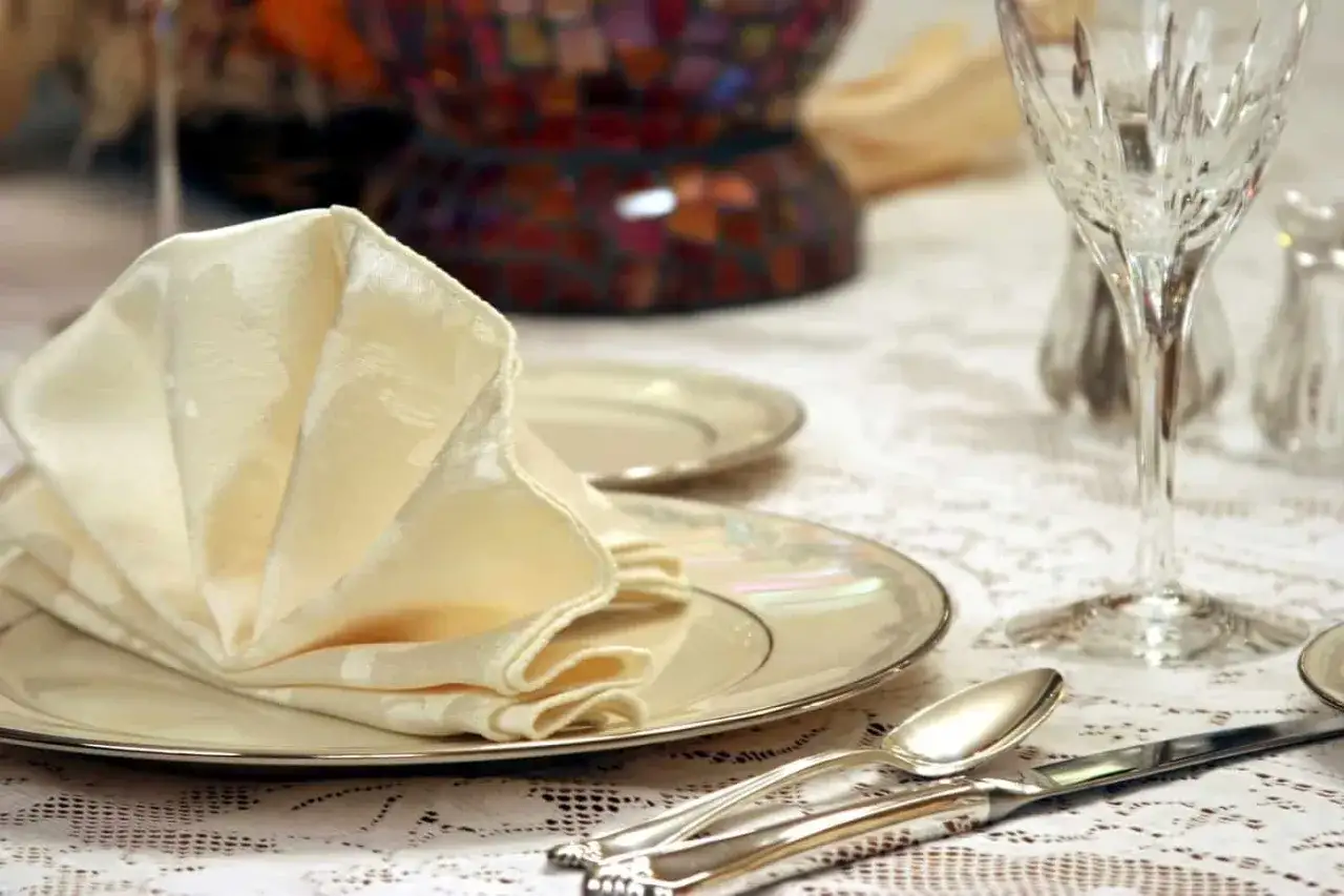 Eine festlich gedeckte Tafel mit elegant gefalteten Servietten, gl&auml;nzendem Besteck und einem geschliffenen Weinglas.
