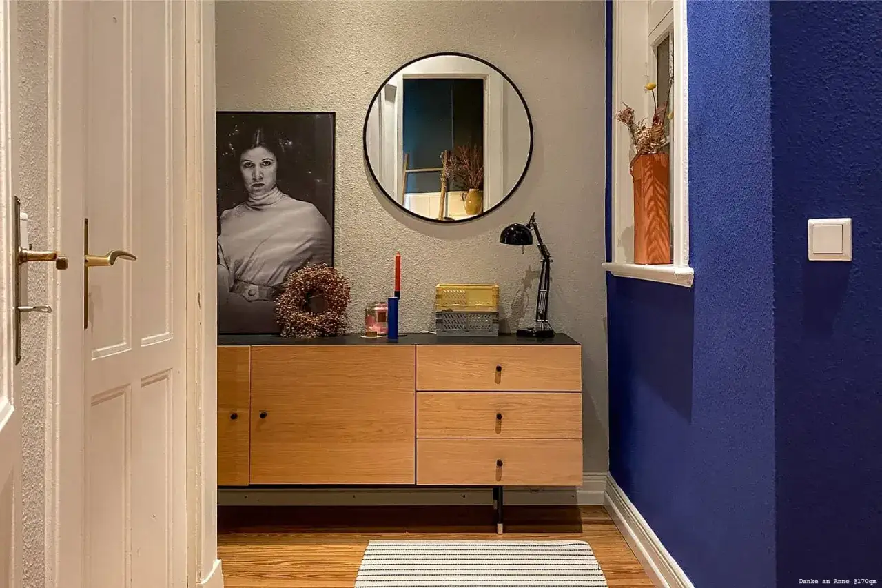 Ein Flur mit einem Bild von Prinzessin Leia, einem runden Spiegel und einem Sideboard. Die Wand ist in einem tiefen Indigo-Farbton gestrichen.