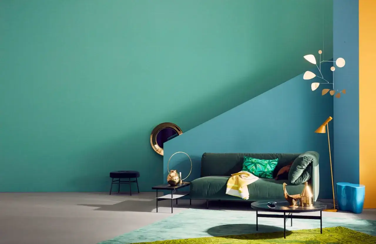 Ein Wohnzimmer mit petrolfarbener Wand, die durch eine blaue Wand und gelbe Akzente ergänzt wird. Welche Farbe passt zu petrol? Hier sehen wir Grün und Gold.