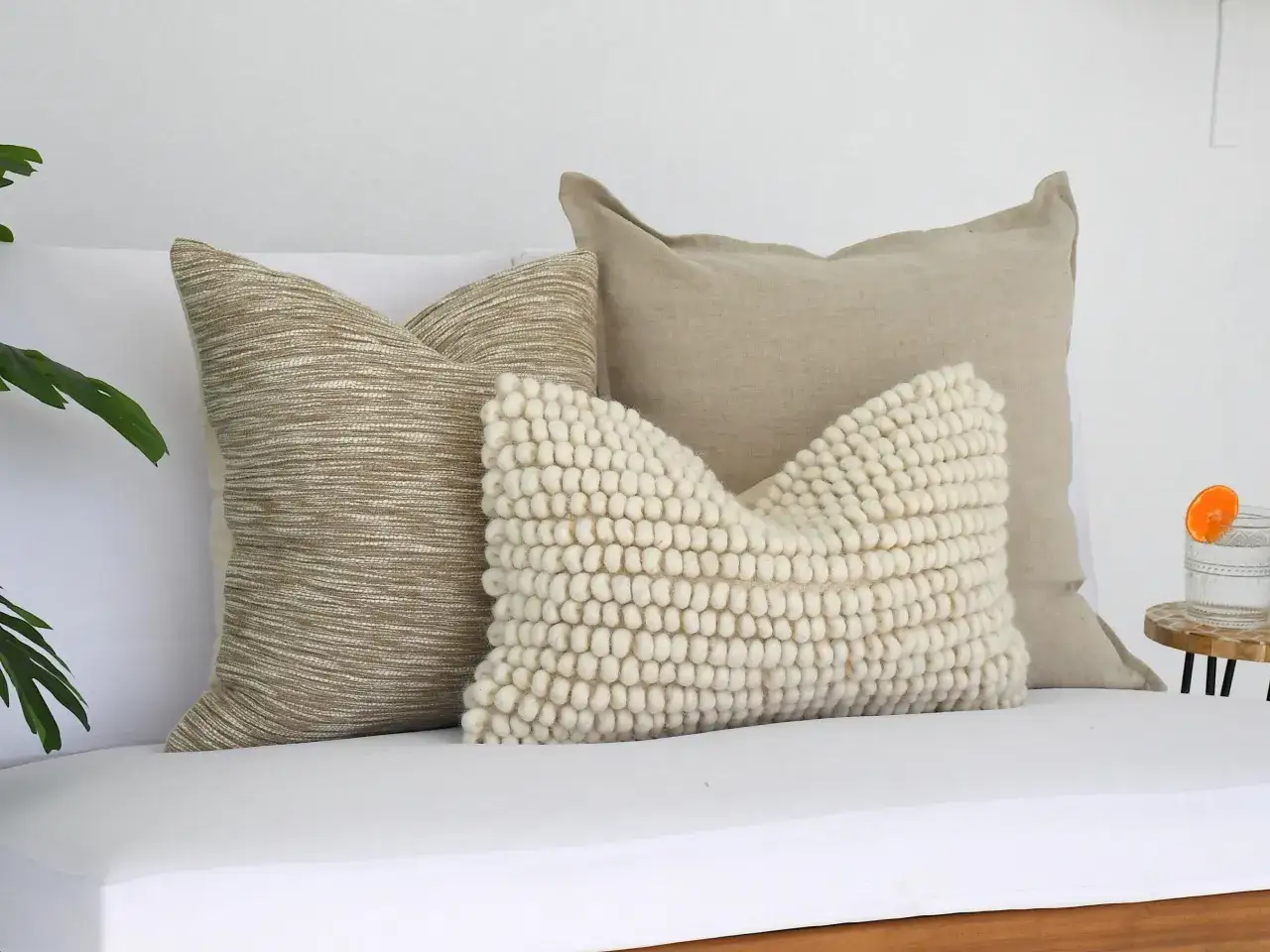 Ein beiges Sofa mit dekorativen Kissen, darunter ein grob gestricktes Wollkissen, l&auml;dt zum Entspannen ein.