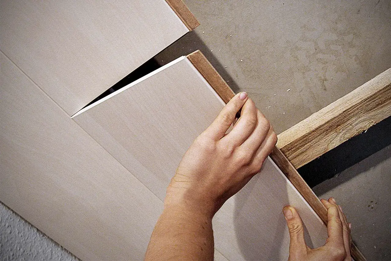 Hände bringen Deckenpaneele an einer Holzleiste an. Die Paneele sind hell und haben eine feine Maserung.