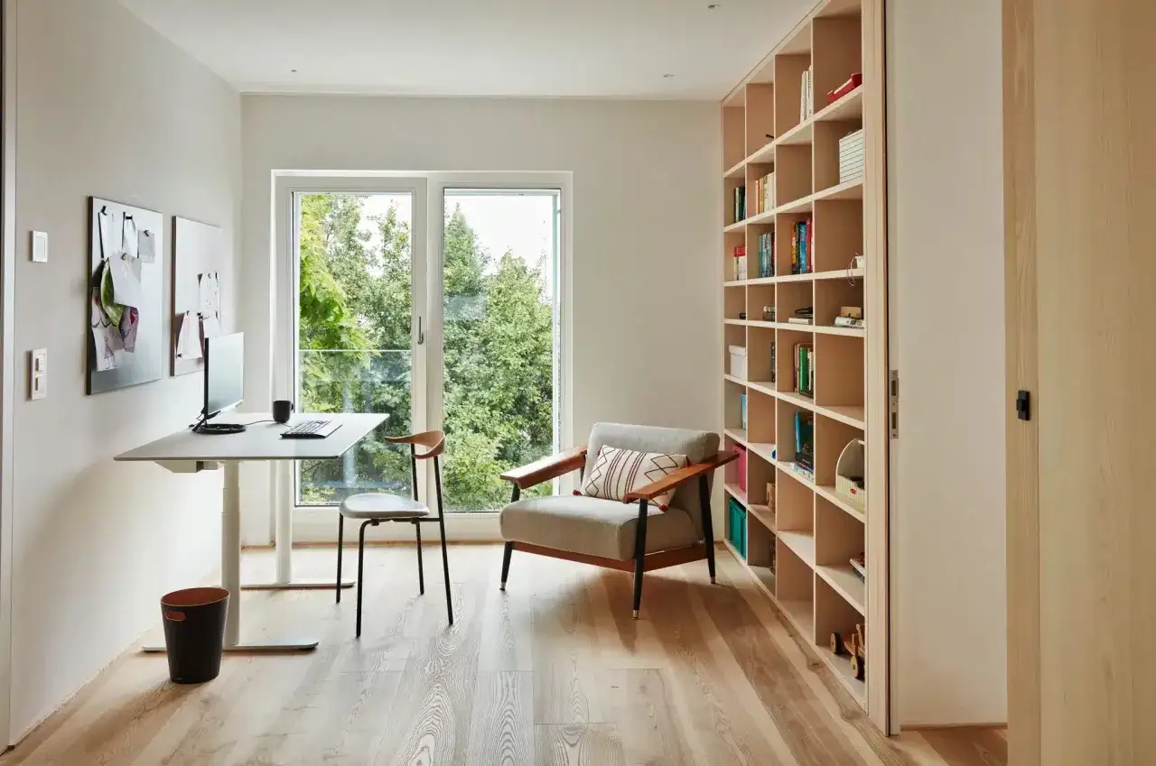 Ein helles, modernes kleines Arbeitszimmer einrichten mit Schreibtisch, Sessel und Bücherregal. Viel Tageslicht durch großes Fenster.