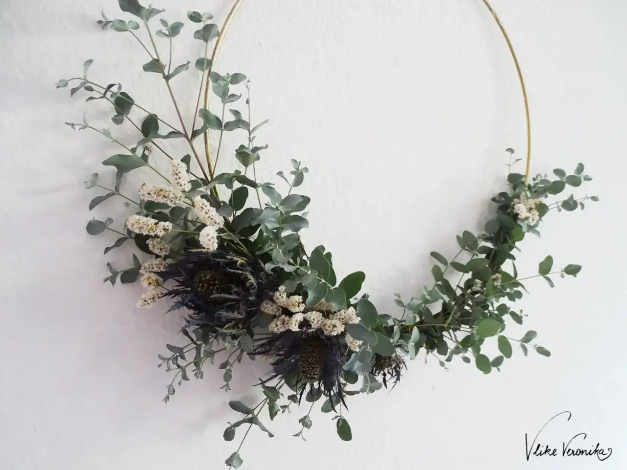 Ein moderner Blumenkranz mit Eukalyptus, kleinen wei&szlig;en Bl&uuml;ten und dunklen Disteln. Das Binden dieses Kranzes ist eine kreative Auszeit.