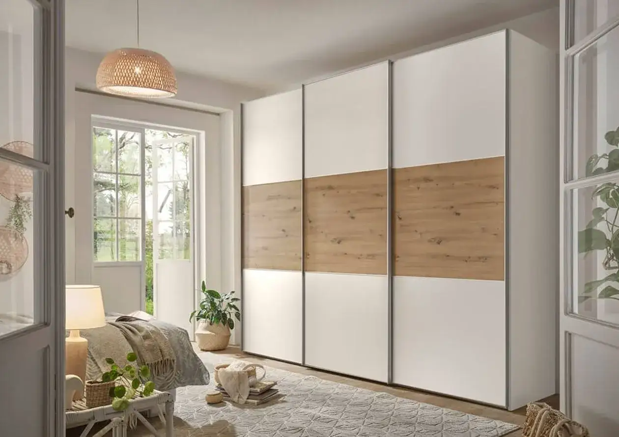 Schlafzimmer beige Ideen: Ein moderner Kleiderschrank mit Holz- und weißen Fronten, daneben ein Bett und ein Fenster mit Blick ins Grüne.