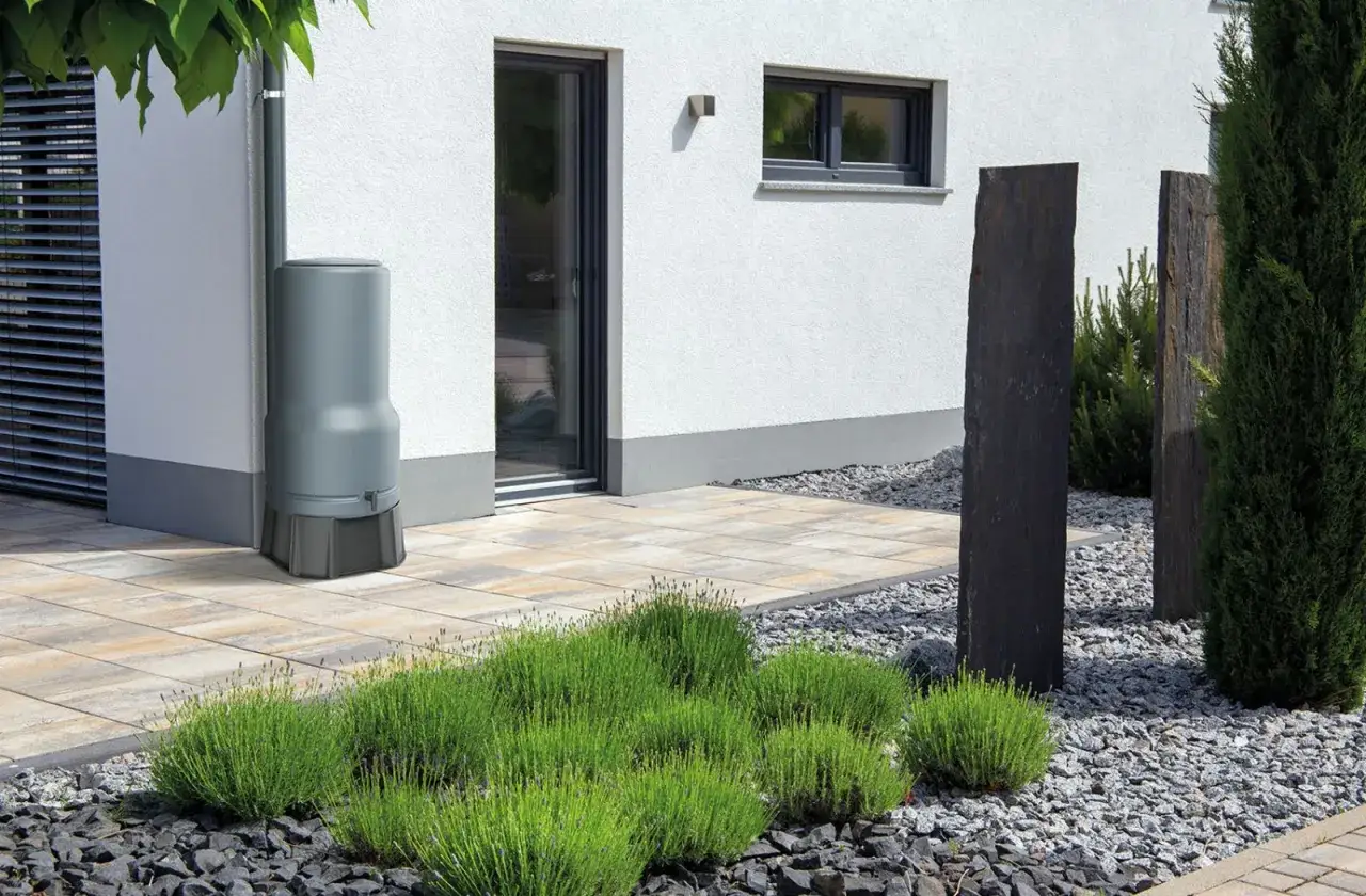 Grauer Regentank neben Hauswand, um Regenwasser aufzufangen. Moderne Terrasse mit Lavendel und Steinsäulen.