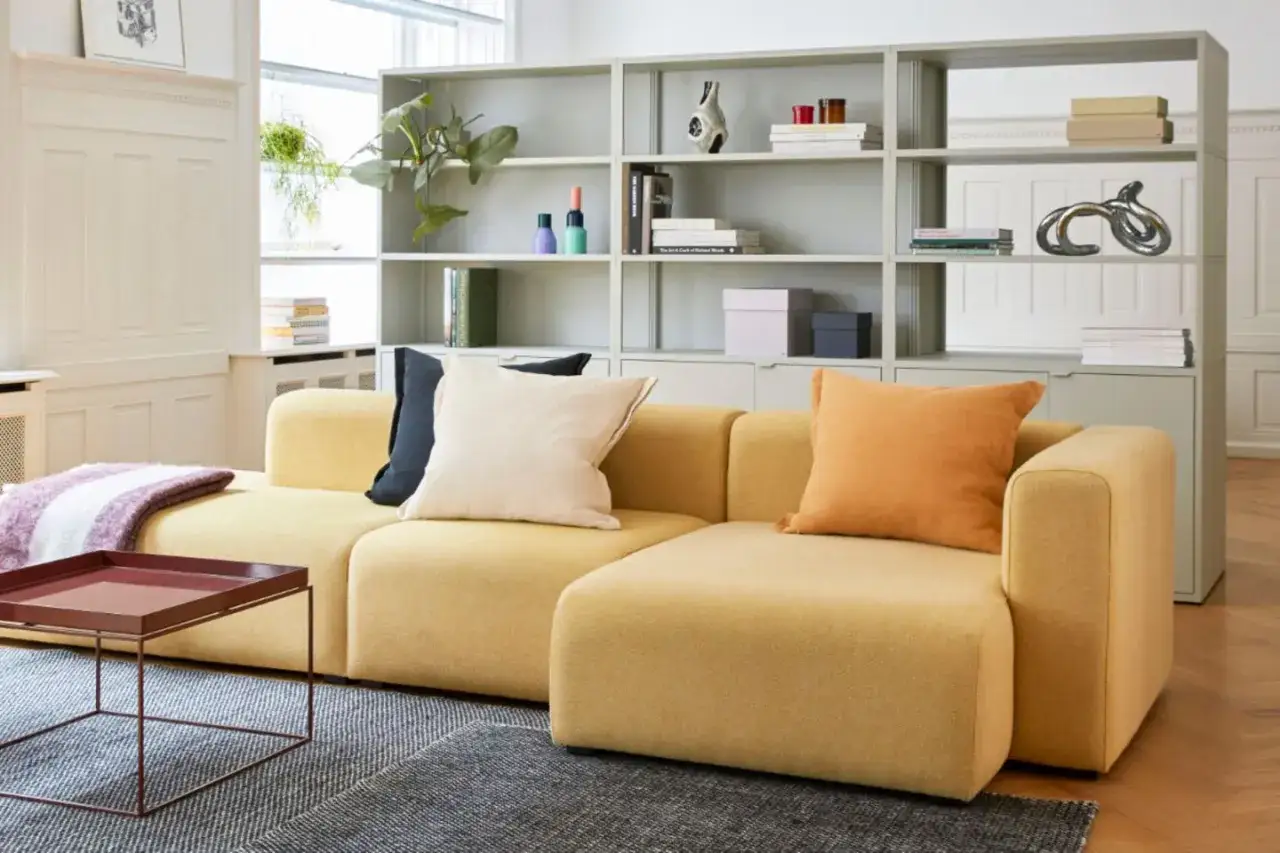 Moderne gelbe Couch als Raumteiler-Idee, mit B&uuml;cherregal im Hintergrund.