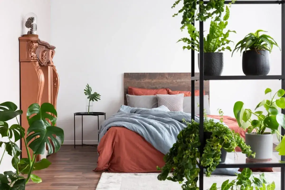Gr&uuml;ne Pflanzen im Schlafzimmer schaffen eine beruhigende Atmosph&auml;re. Ein Bett mit rustikalem Kopfteil und erdigen T&ouml;nen wird von &uuml;ppigem Gr&uuml;n umrahmt.