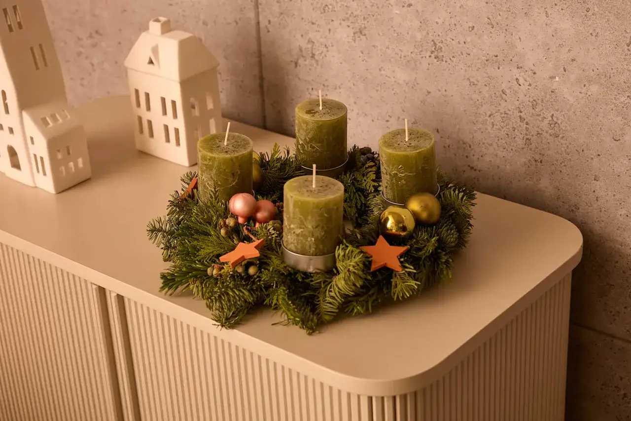 Ein ausgefallener Adventskranz mit vier grünen Kerzen, Tannenzweigen, goldenen Kugeln und Sternen.