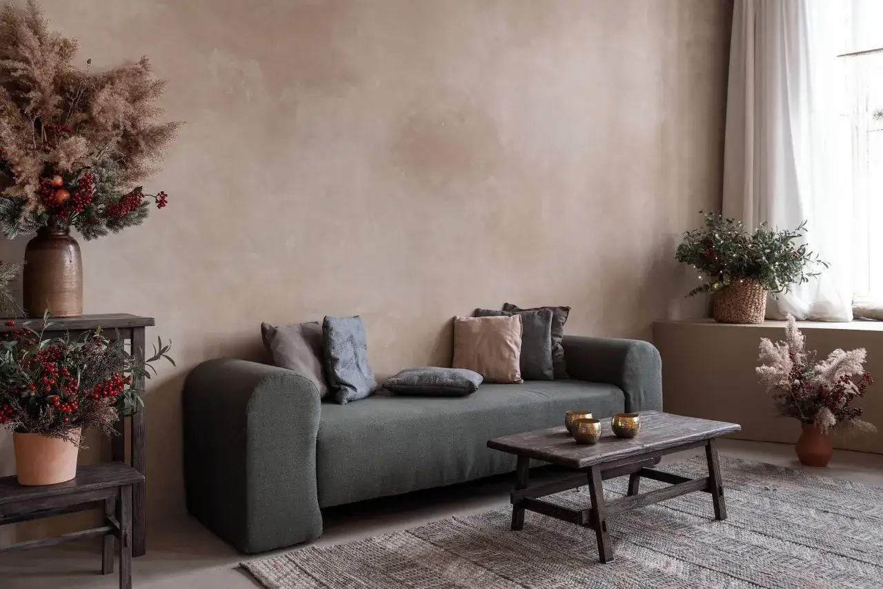 Gem&uuml;tliches Wohnzimmer mit Sofa, Holztisch und rustikaler Wand in limewash technik. Dekoration mit Trockenblumen und Beeren.