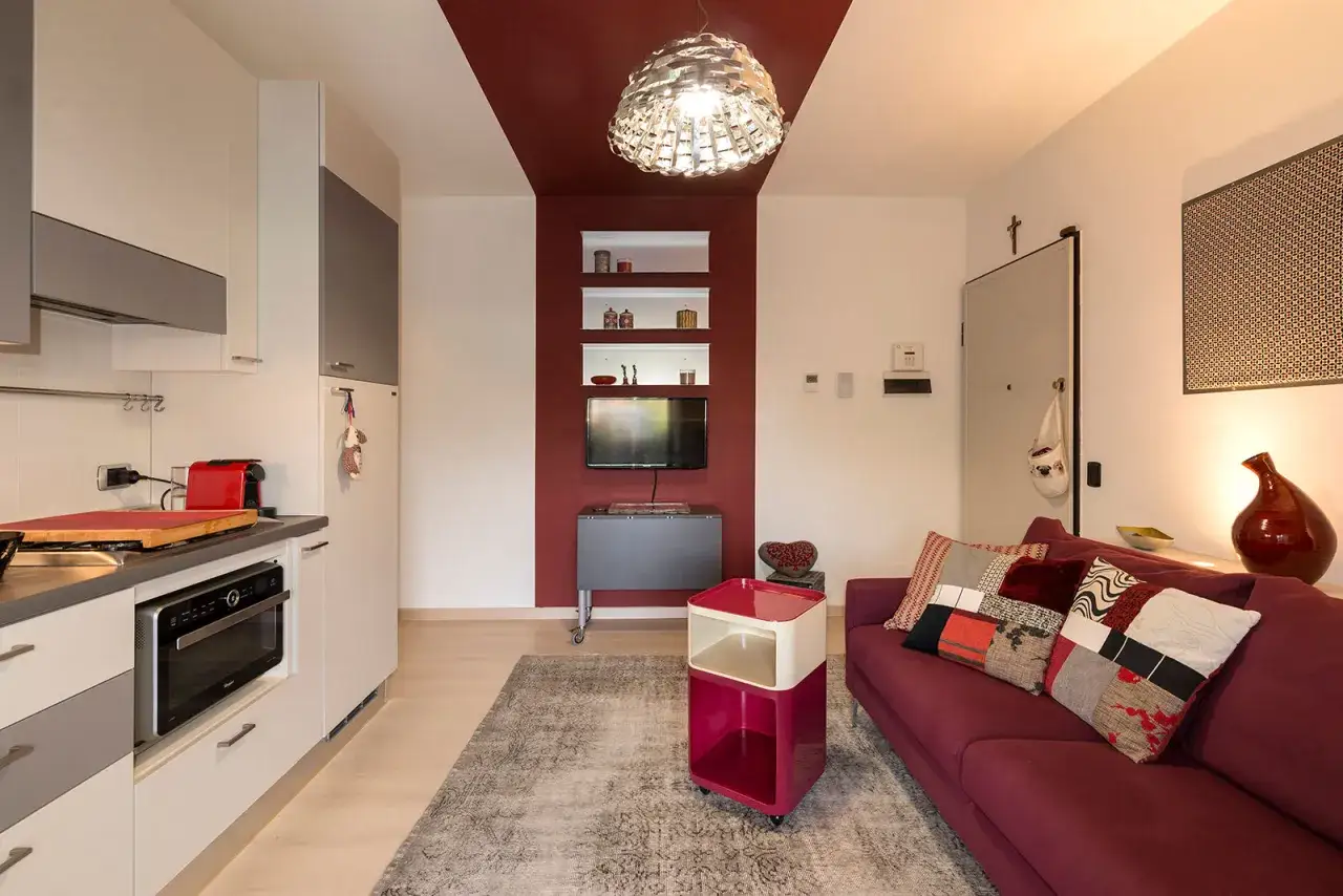 Ein Wohnzimmer mit bordeauxroter Couch und Kissen. Die Frage, welche Farbe passt zu bordeaux, wird durch die Wandgestaltung und Dekoration beantwortet.