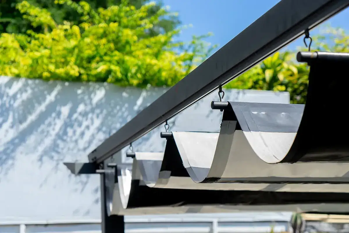 Sonnensegel befestigen Ideen: Ein ausziehbarer Sonnenschutz mit Stoffbahnen, die an einer Pergola-Konstruktion hängen.