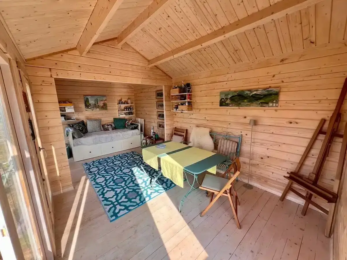 Gemütliches kleines gartenhaus innen gestalten: Tagesbett, Tisch mit Stühlen, Staffelei und Bilder schaffen eine kreative Oase.