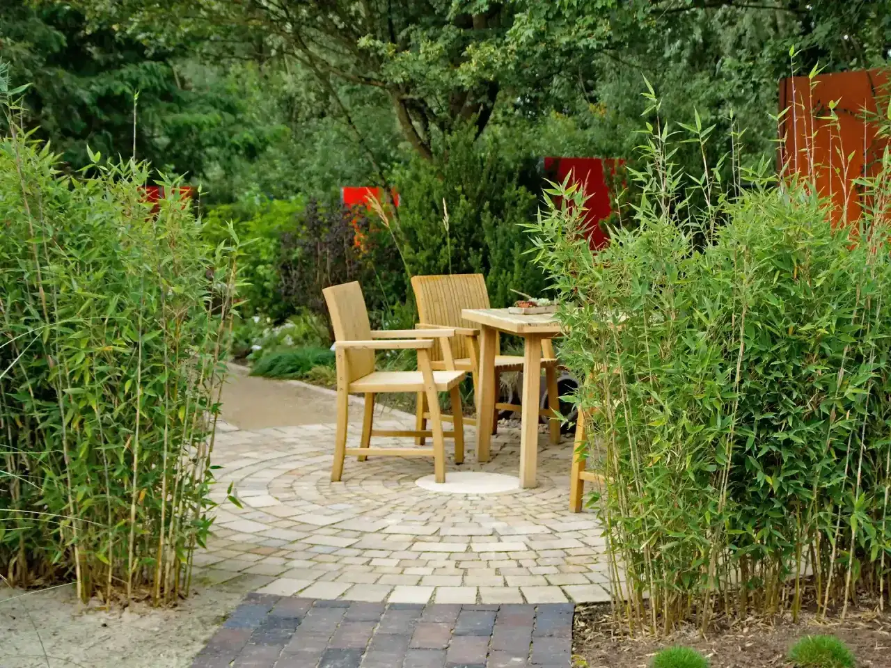 Ein Garten mit Bambus einpflanzen, der einen Sitzbereich mit Holztisch und Stühlen umrahmt.