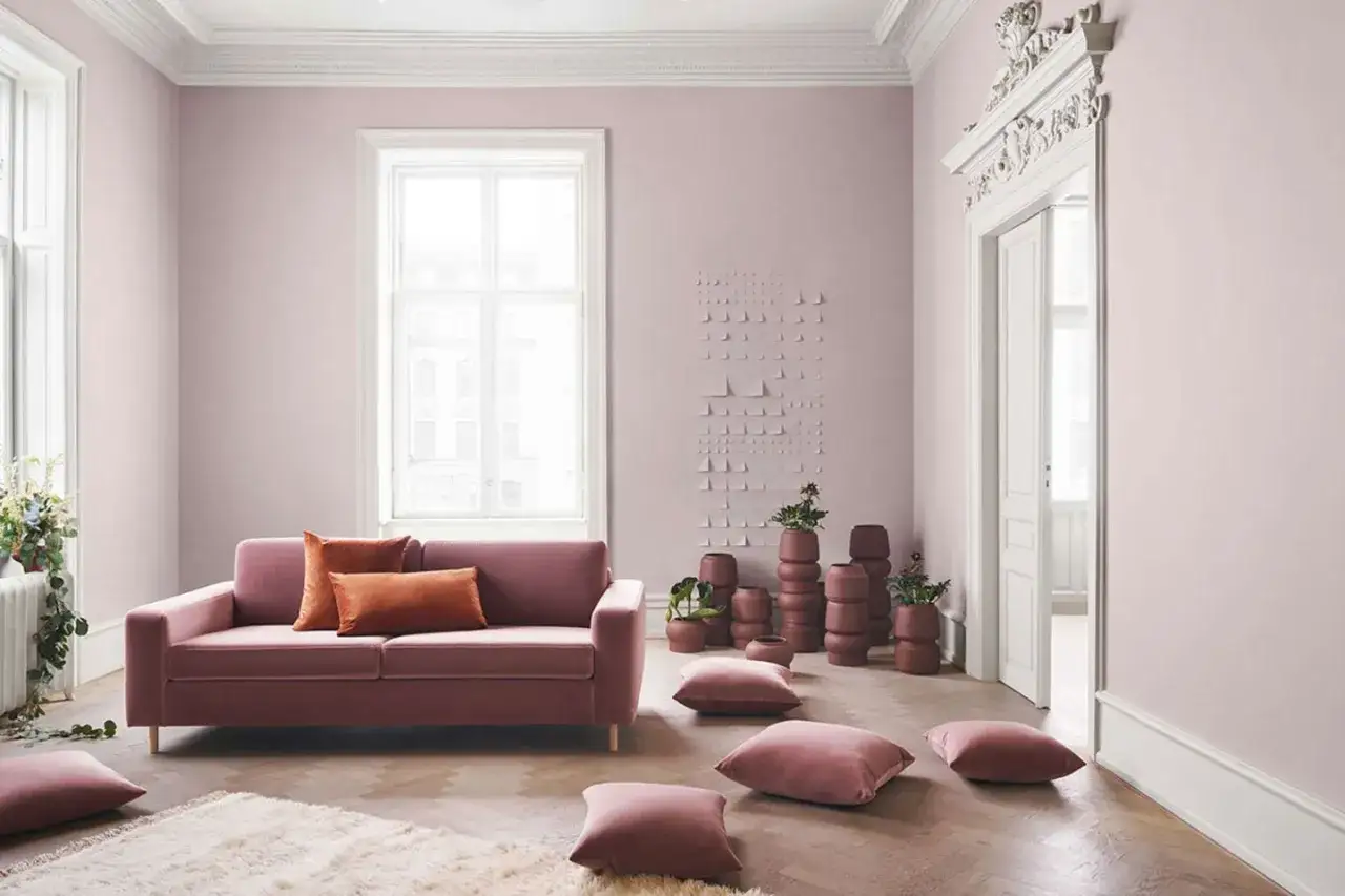 Ein rosafarbenes Sofa mit Kissen in warmen Erdt&ouml;nen. Die W&auml;nde sind in einem zarten Rosa gestrichen, was zeigt, welche Farbe passt zu Rosa: warme T&ouml;ne.