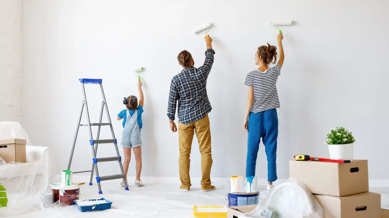 Familie streicht gemeinsam die Wohnung weiß. Vater, Mutter und Kind arbeiten mit Rollen an der Wand.