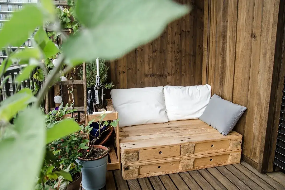 Gem&uuml;tliche Lounge-Ecke auf einer schmalen Terrasse gestalten: Paletten-Sofa mit Kissen, Pflanzen und Kerzen.