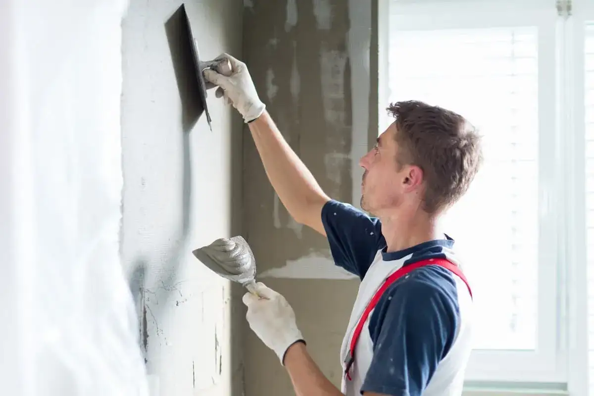 Mann verputzt eine Wand mit Kelle und Gl&auml;tter. So lernt man, wie man eine Wand verputzt.