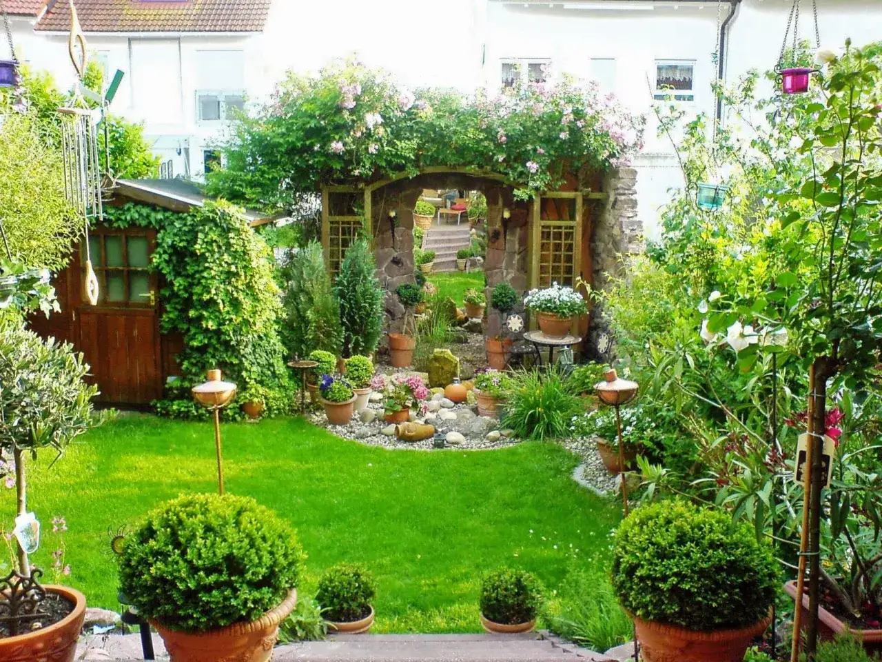 Ein moderner kleiner Garten im Reihenhaus mit Steinbogen, Rosen, Buchsbaumkugeln und einer gem&uuml;tlichen Sitzecke.