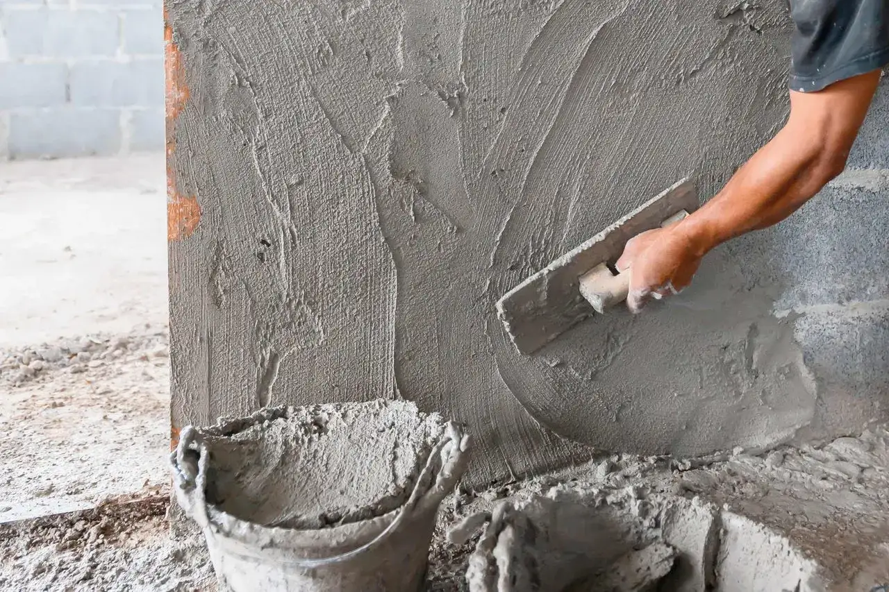 Hand gl&auml;ttet frischen M&ouml;rtel auf eine Wand. Der Unterschied zwischen Beton und Zement wird hier deutlich, da Zement als Bindemittel dient.