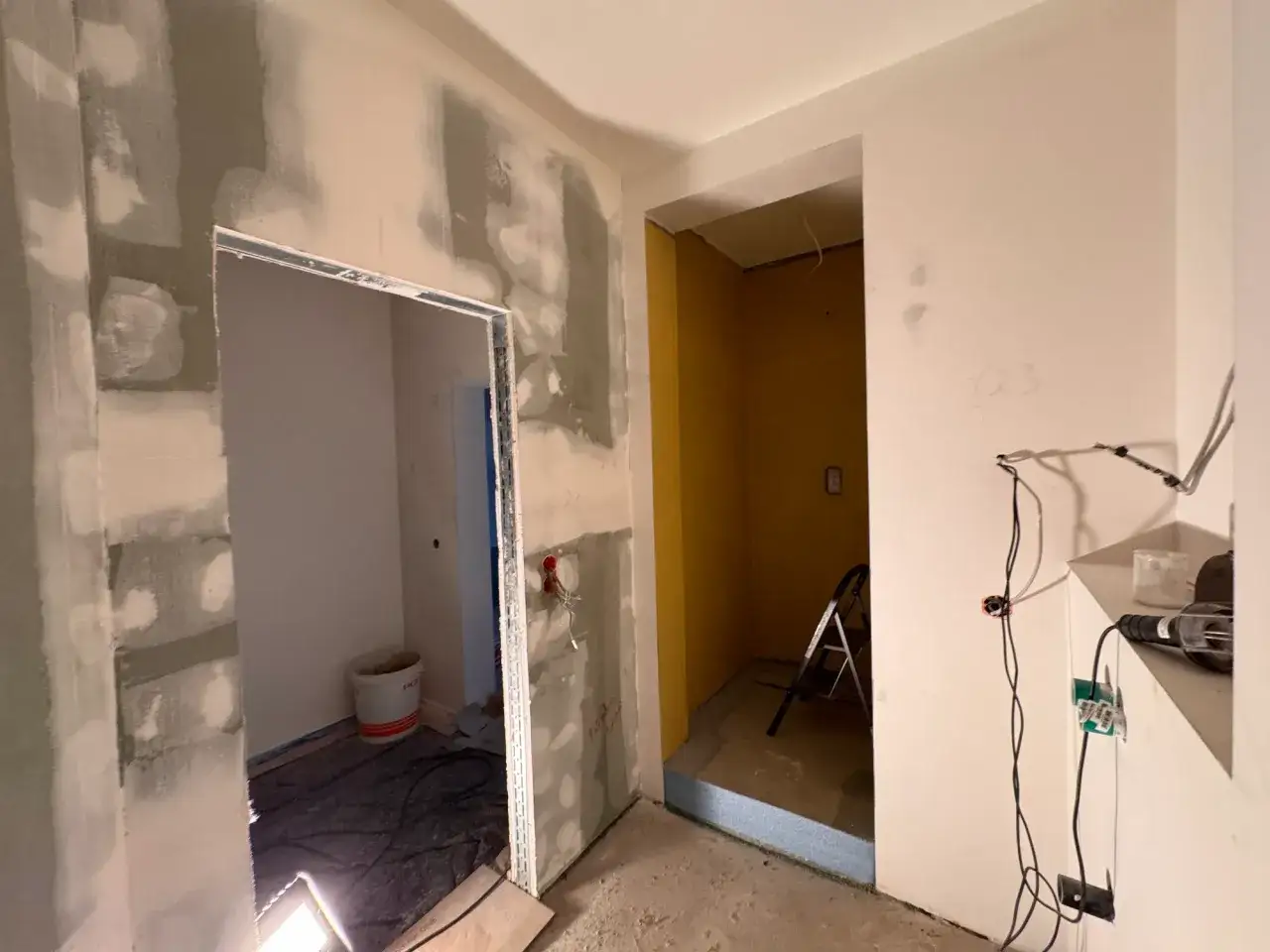 Bau einer Trennwand im Gange. Gipskartonplatten sind angebracht, Spachtelmasse trocknet. Ein Eimer und Werkzeug liegen bereit.