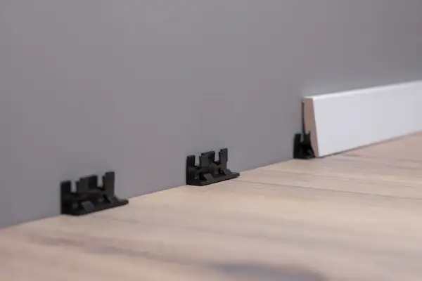 Schwarze Clips zur einfachen Montage von Sockelleisten an der Wand.