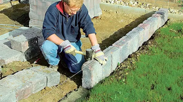 Mann setzt mit Hammer und Richtschnur präzise Rasenkantensteine, um den Garten zu gestalten.