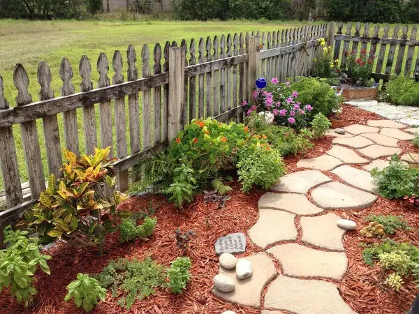 Natürliche Steinplatten formen einen geschwungenen Gartenweg, umgeben von bunten Blumen und grünen Pflanzen. Tolle Gartenweg Ideen für Ihr Zuhause.