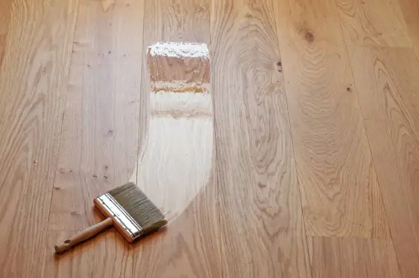 Breite Pinsel trägt Lack auf einen hellen Holzdielenboden auf. Der Prozess, einen Dielenboden zu versiegeln, beginnt.