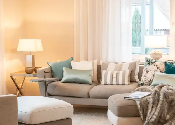 Ein beiges Sofa mit vielen Kissen, darunter gestreifte und florale Muster, lädt zum Entspannen ein.