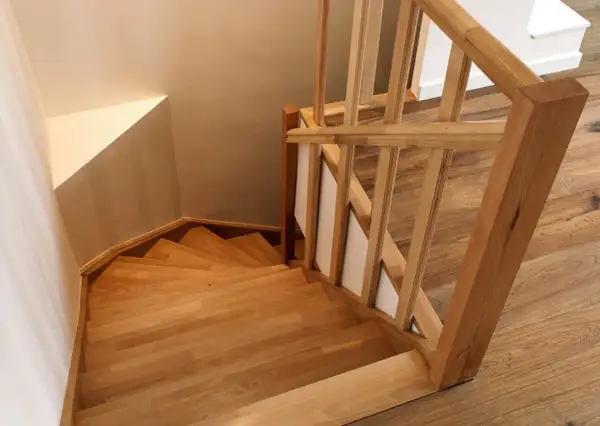 Holztreppe mit geschwungenen Treppenstufen. Der Handlauf und die Stufen sind aus hellem Holz gefertigt, was den Eindruck von Wärme und Natürlichkeit vermittelt. Die Treppenstufen streichen ist hier nicht nötig, da das Holz bereits schön zur Geltung kommt.