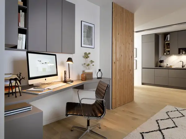 Moderne homeoffice ideen: Ein aufgeräumter Schreibtisch mit iMac, Lederstuhl und Regalwand. Daneben eine Holzwand, die in eine Küche übergeht.