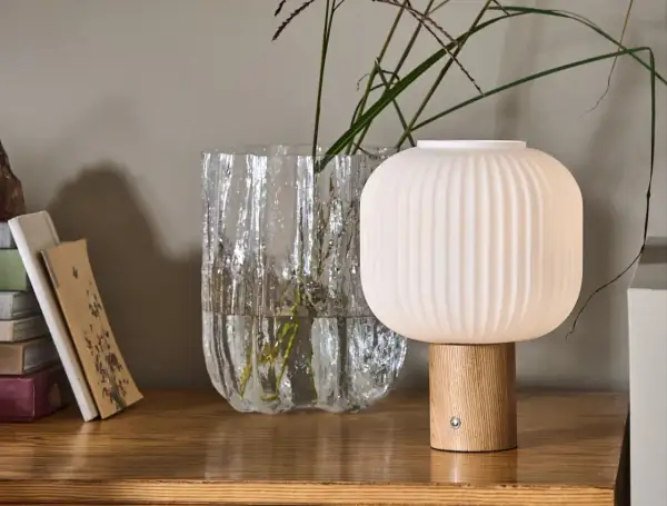 Eine skandinavische tischlampe holz mit geripptem Schirm und Holzfuß steht neben einem Glasvase mit Gräsern.