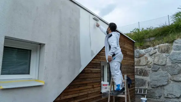 Mann streicht mit Rolle eine Hausfassade. So streicht man eine Fassade: Schritt für Schritt zum neuen Look.