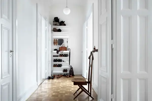 Helle Türen und ein weißes Regal lassen den schmalen Flur optisch breiter wirken. Schuhe und Hüte sind ordentlich verstaut.