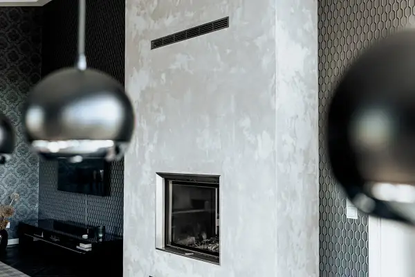Edler Kamin mit Wischtechnik Wand in Grau. Daneben eine Wand mit geometrischem Muster und ein Teil einer Hängeleuchte.